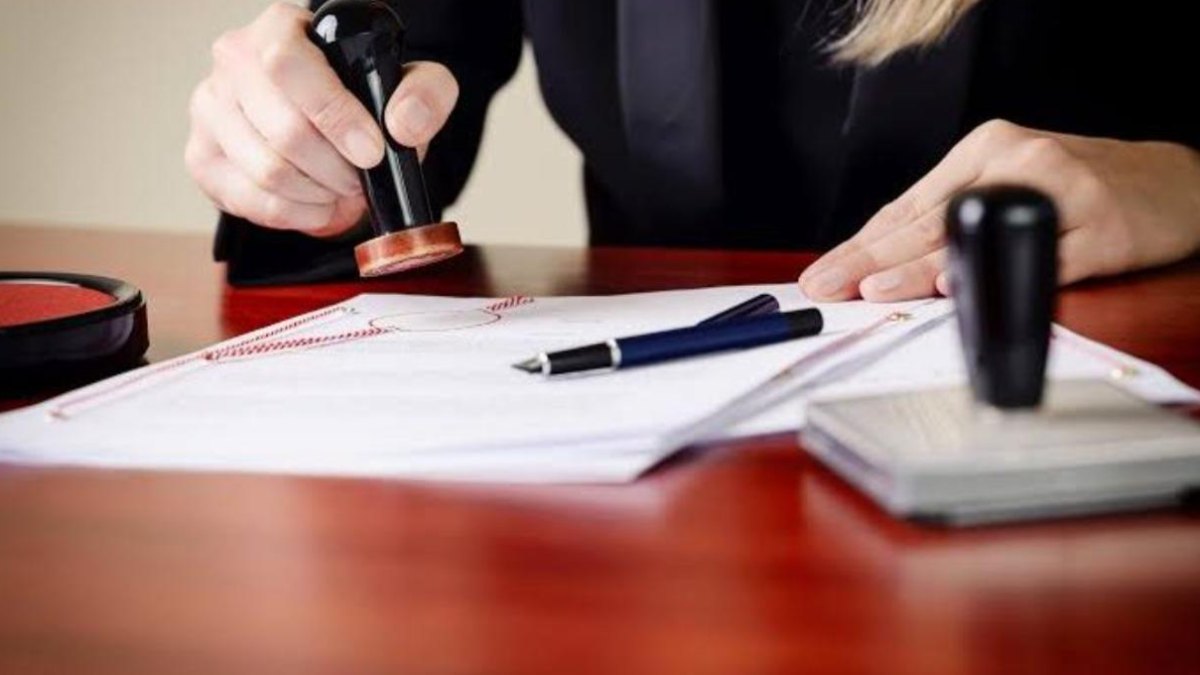 A notary stamping a document with a fountain pen and a second stamp on the desk