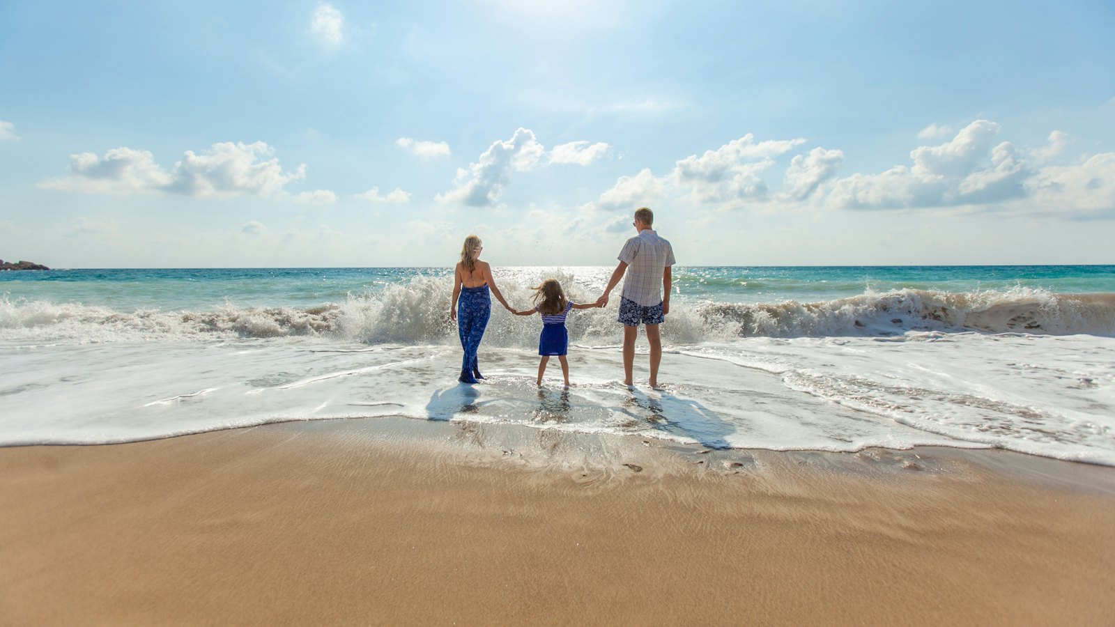Vader, moeder en dochter hand in hand aan de waterlijn van een tropisch strand